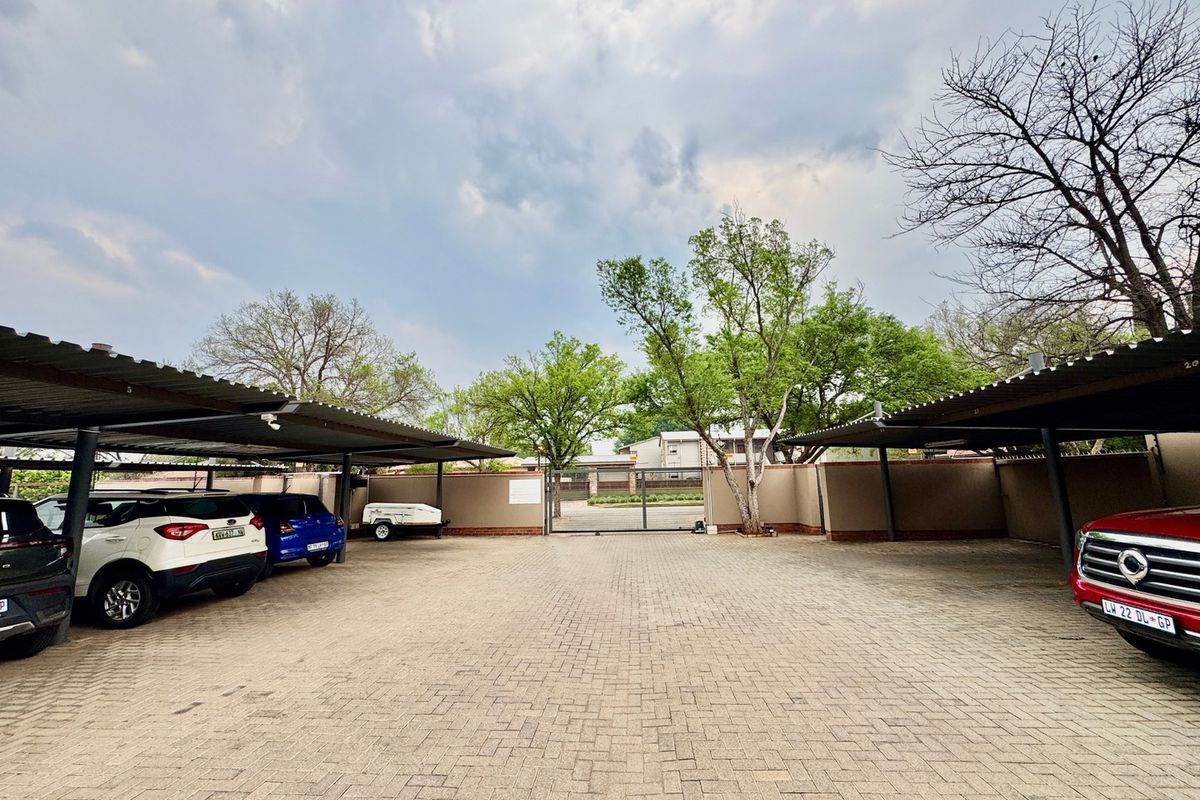 A well-maintained paved parking area featuring covered parking bays, perimeter walling, and a secure gated entrance.