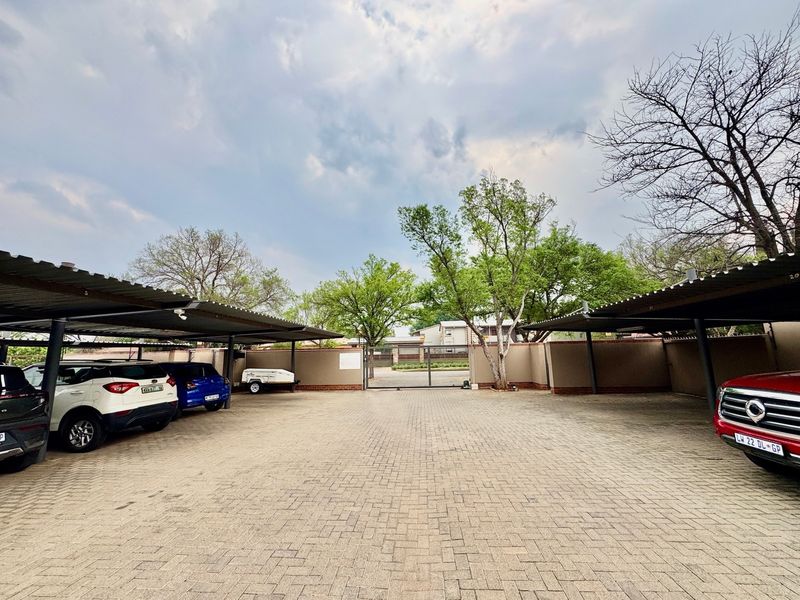 A well-maintained paved parking area featuring covered parking bays, perimeter walling, and a secure gated entrance.
