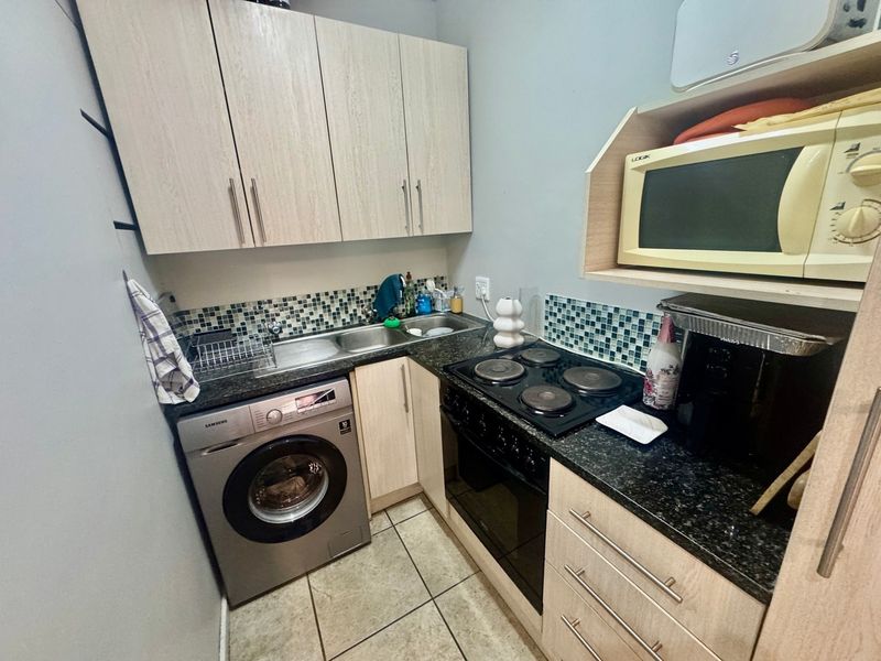 Compact kitchen featuring light wood-look cabinetry, granite countertops, mosaic tile backsplash, and integrated electric cooking appliances.