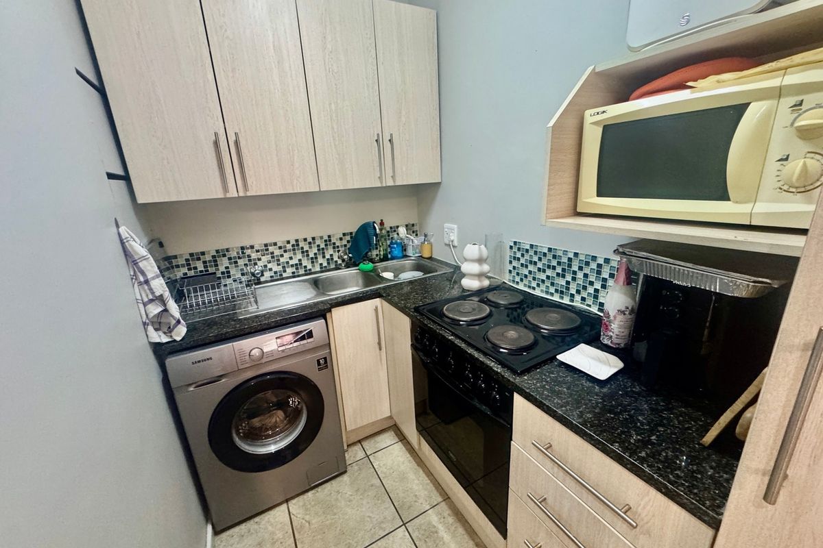 Compact kitchen featuring light wood-look cabinetry, granite countertops, mosaic tile backsplash, and integrated electric cooking appliances.