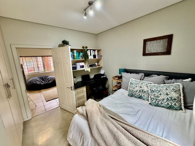 A well-lit bedroom featuring built-in cupboards, tiled flooring, and an adjoining space, offering a functional layout with neutral wall finishes.