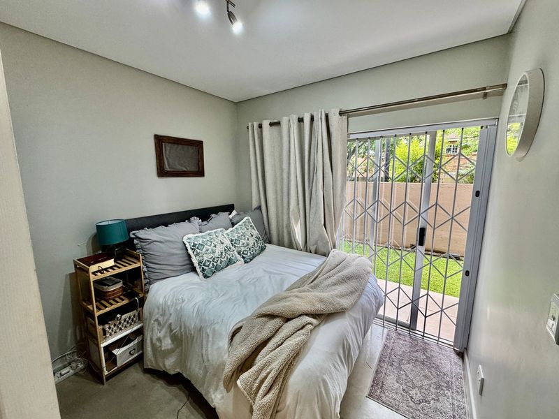 A cozy bedroom featuring a sliding glass door with a security gate, providing direct access to the outdoor area and natural light.