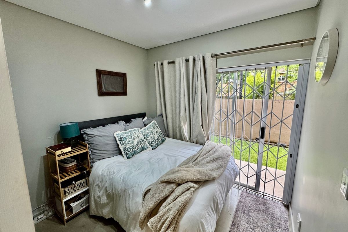 A cozy bedroom featuring a sliding glass door with a security gate, providing direct access to the outdoor area and natural light.