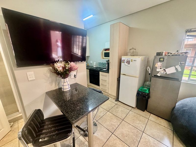 Compact open-plan kitchen and living area featuring tiled flooring, built-in cabinetry, and integrated cooking appliances.