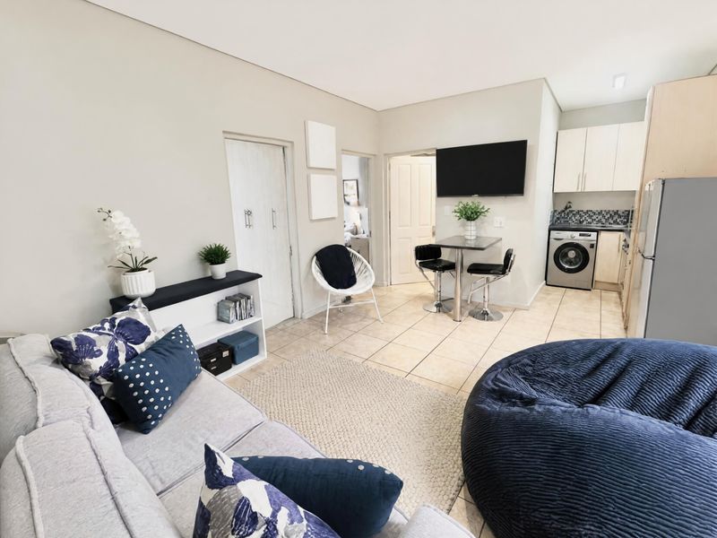 Open-plan living area featuring tiled flooring, a compact kitchen with built-in cabinetry, and integrated laundry facilities, creating a functional and cohesive living space.