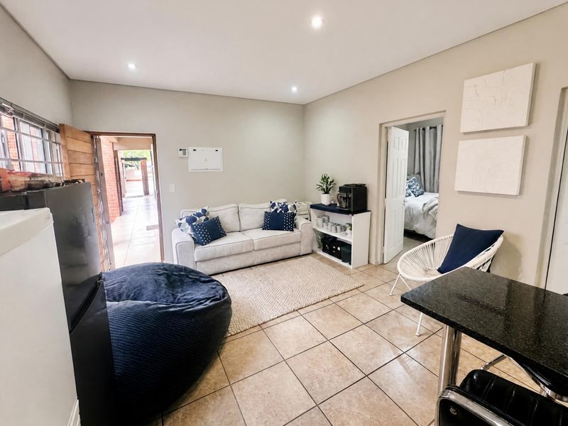 Open-plan living area featuring neutral tiled flooring, recessed downlighting, and direct access to an exterior walkway and adjacent bedroom.