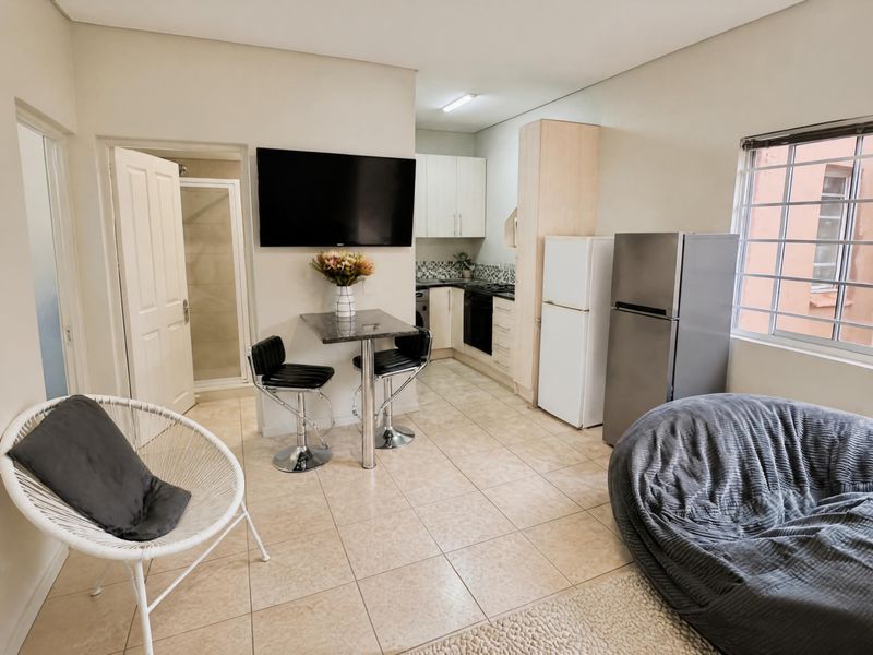 Open-plan living area featuring a compact kitchen with built-in cabinetry, tiled flooring, and an adjacent bathroom with a shower enclosure.