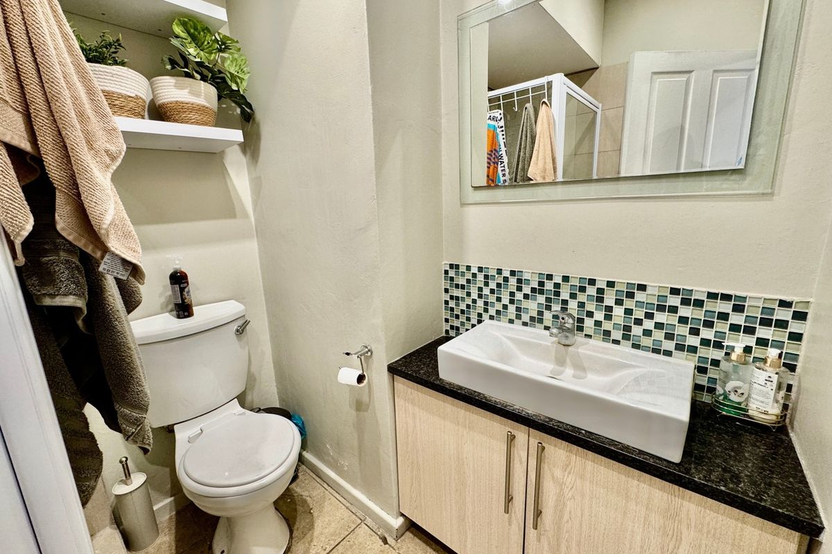 A functional bathroom featuring a modern vessel sink on a vanity cabinet, mosaic tile backsplash, wall-mounted mirror, and floating shelving.