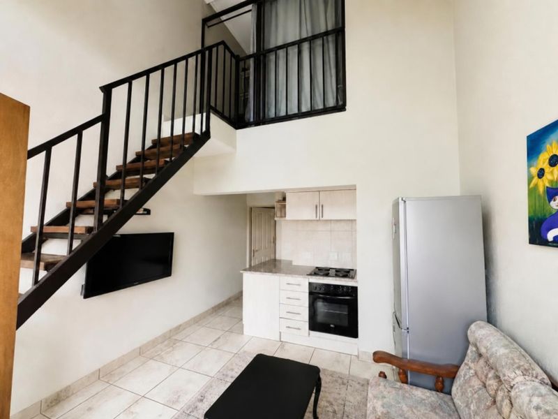 Open-plan living area featuring a compact kitchen with built-in appliances and a staircase leading to a mezzanine level.