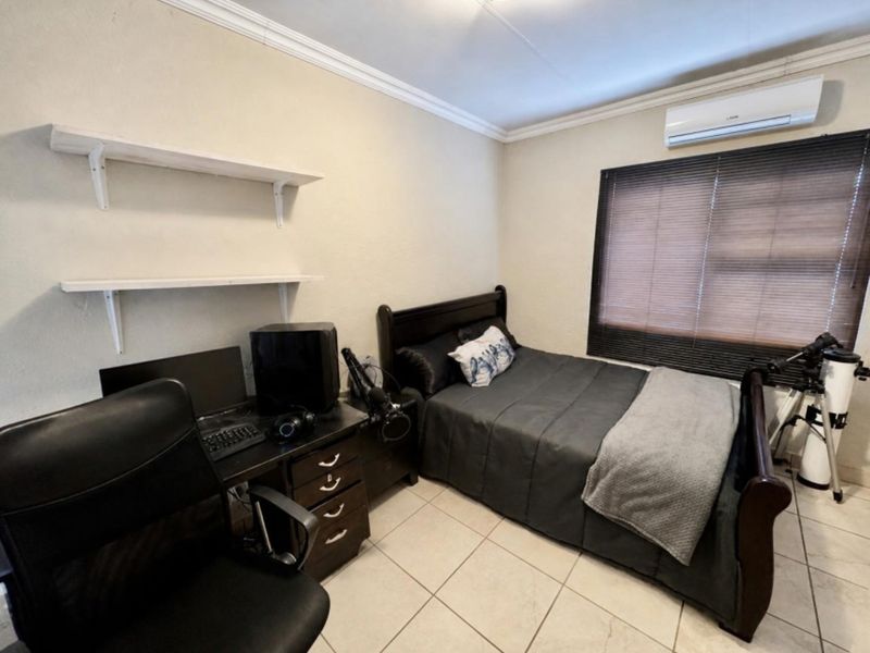 A well-maintained bedroom featuring tiled flooring, crown molding, wall-mounted shelving, and a split-system air conditioning unit.