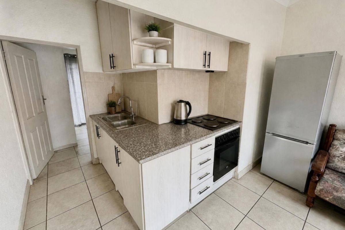 A compact kitchen featuring light-toned cabinetry, granite-look laminate countertops, a built-in oven and hob, and neutral floor tiling.