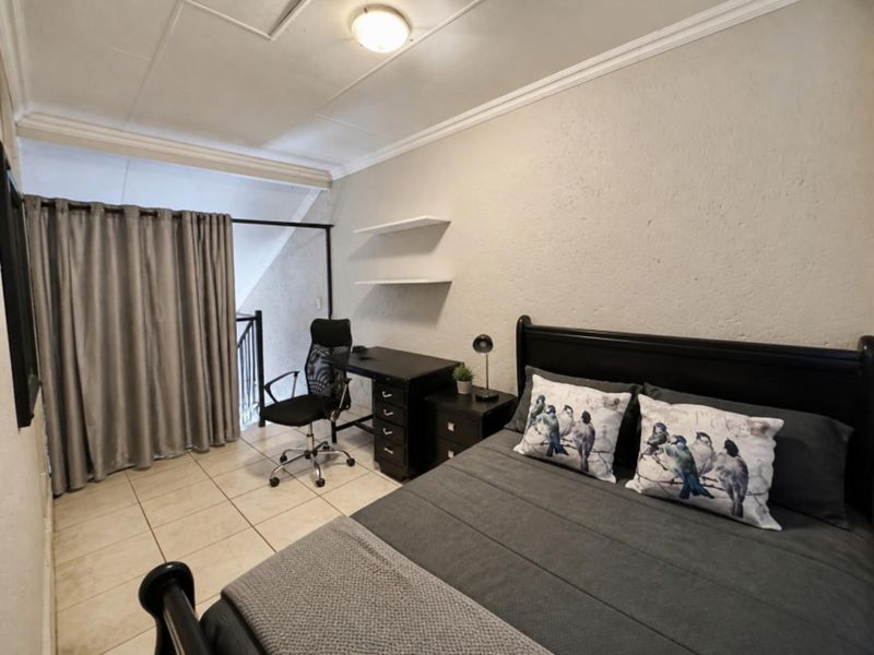 A bedroom featuring tiled flooring, crown molding, and built-in shelving, with an open-plan layout overlooking a staircase area.
