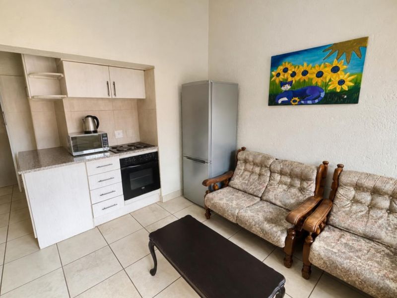 Compact open-plan living area featuring a kitchenette with built-in cabinetry, oven, and hob, finished with neutral tiled flooring.