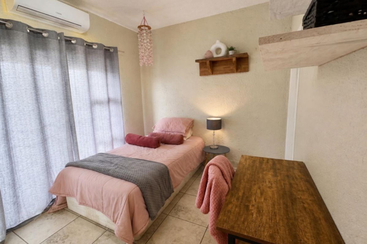 A compact bedroom featuring tiled flooring, a wall-mounted split-system air conditioner, and a sliding glass door providing natural light.