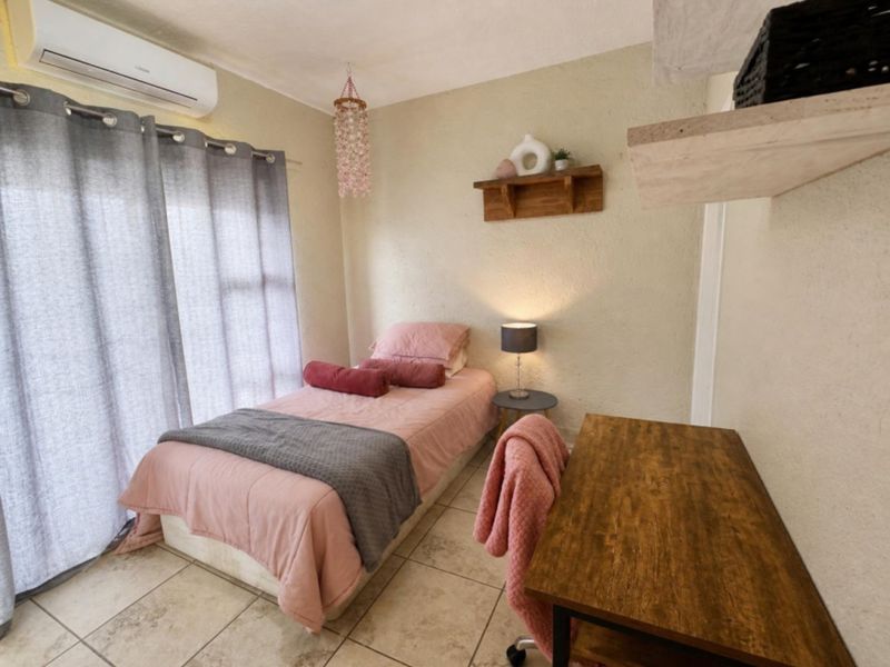 A compact bedroom featuring tiled flooring, a wall-mounted split-system air conditioner, and a sliding glass door providing natural light.