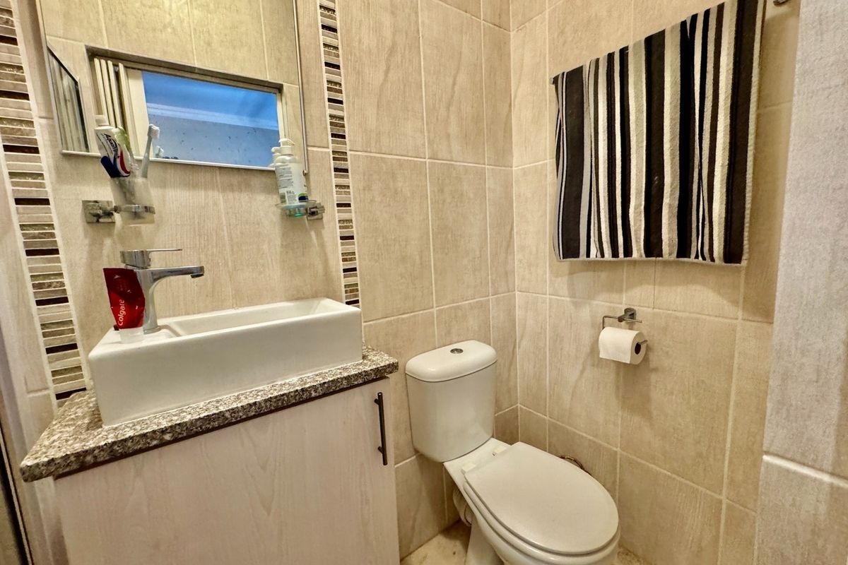 A compact bathroom featuring neutral ceramic wall and floor tiles, a vanity cabinet with a granite countertop, and a modern basin.