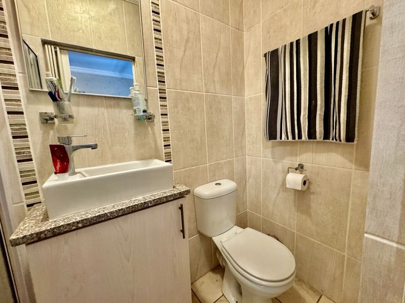 A compact bathroom featuring neutral ceramic wall and floor tiles, a vanity cabinet with a granite countertop, and a modern basin.