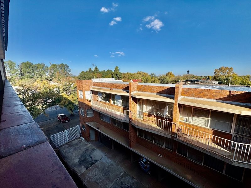 An elevated view of the rear exterior of a brick apartment building, featuring balconies, a concrete driveway, and a metal security gate.