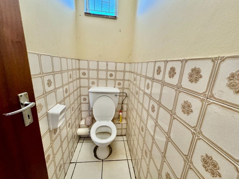 A compact, dated bathroom featuring patterned ceramic wall tiles, a standard toilet, and a small high-level window, requiring modernization and cosmetic updates.