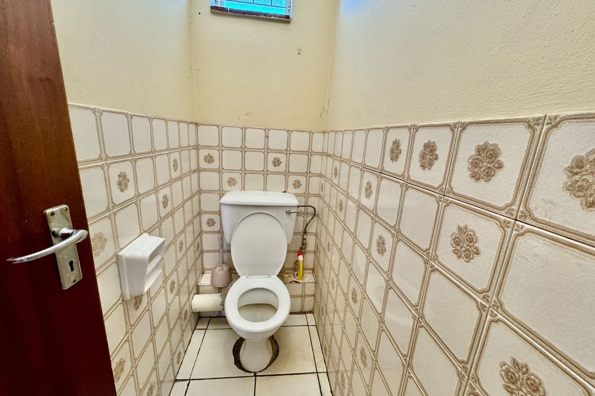 A compact, dated bathroom featuring patterned ceramic wall tiles, a standard toilet, and a small high-level window, requiring modernization and cosmetic updates.