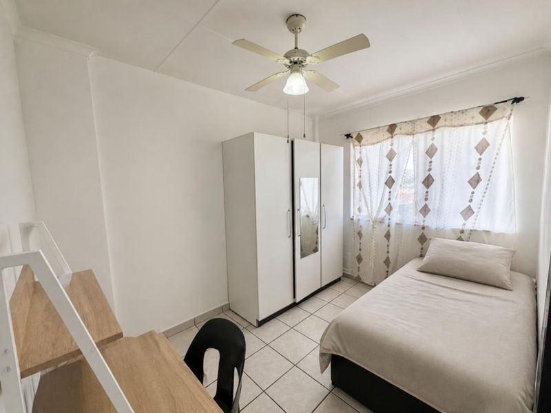 A functional bedroom featuring tiled flooring, a ceiling fan, and a built-in wardrobe, offering a clean and practical living space.