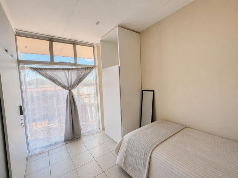 A bright bedroom featuring tiled flooring, a built-in wardrobe, and a large window with access to a balcony area.
