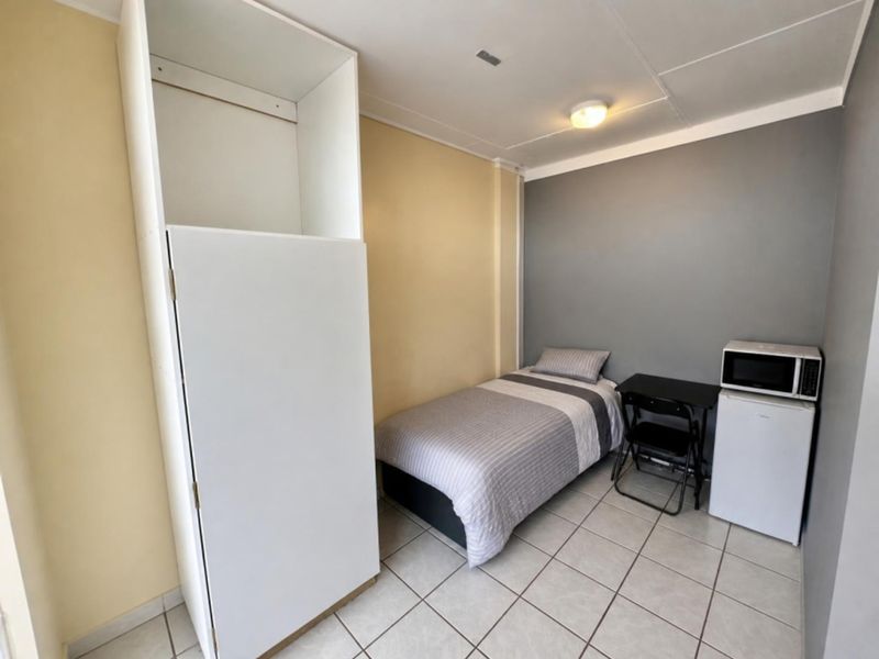 A compact bedroom featuring tiled flooring, a built-in cupboard, and neutral wall tones, offering a functional living space.