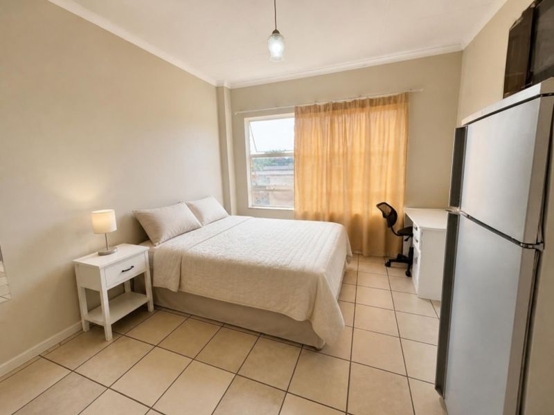 A functional bedroom featuring tiled flooring, neutral wall finishes, and a large window providing natural light.
