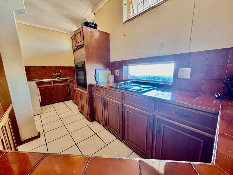A dated kitchen featuring wooden cabinetry, tiled countertops, an integrated oven and hob, and tiled flooring, requiring cosmetic updates to modernize the space.