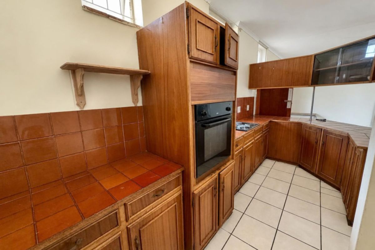 A dated kitchen featuring wooden cabinetry, tiled countertops, and built-in oven, offering a functional layout ready for modern renovation.