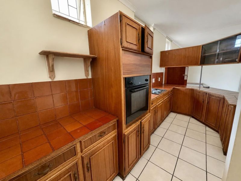 A dated kitchen featuring wooden cabinetry, tiled countertops, and built-in oven, offering a functional layout ready for modern renovation.