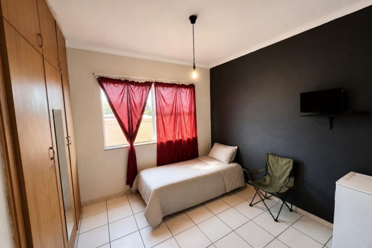 A functional bedroom featuring built-in wooden cupboards, tiled flooring, and a dark accent wall, providing a neutral base for personalization.