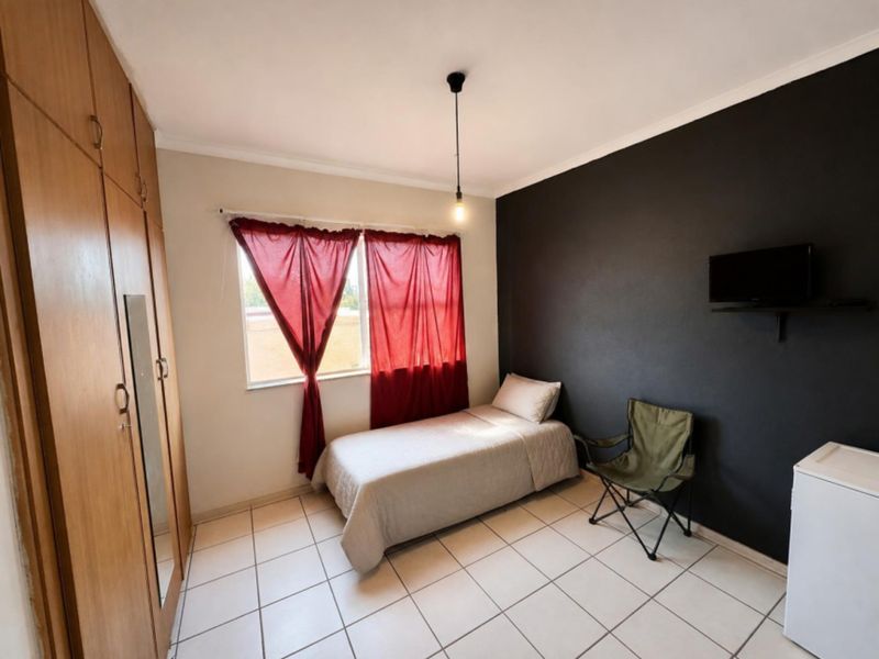 A functional bedroom featuring built-in wooden cupboards, tiled flooring, and a dark accent wall, providing a neutral base for personalization.