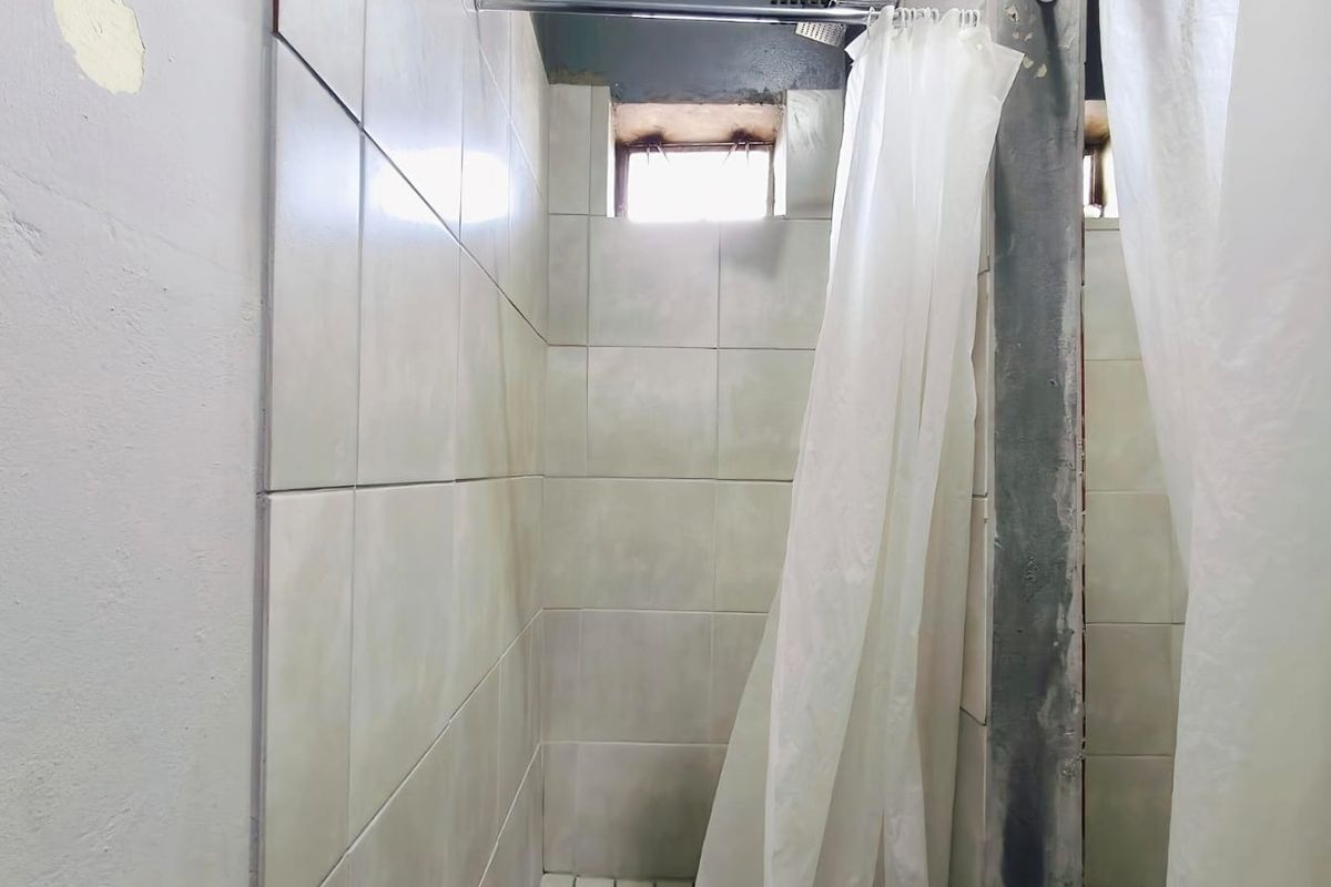A basic shower area featuring tiled walls and a small window, currently in need of maintenance and cosmetic updates to improve its condition.