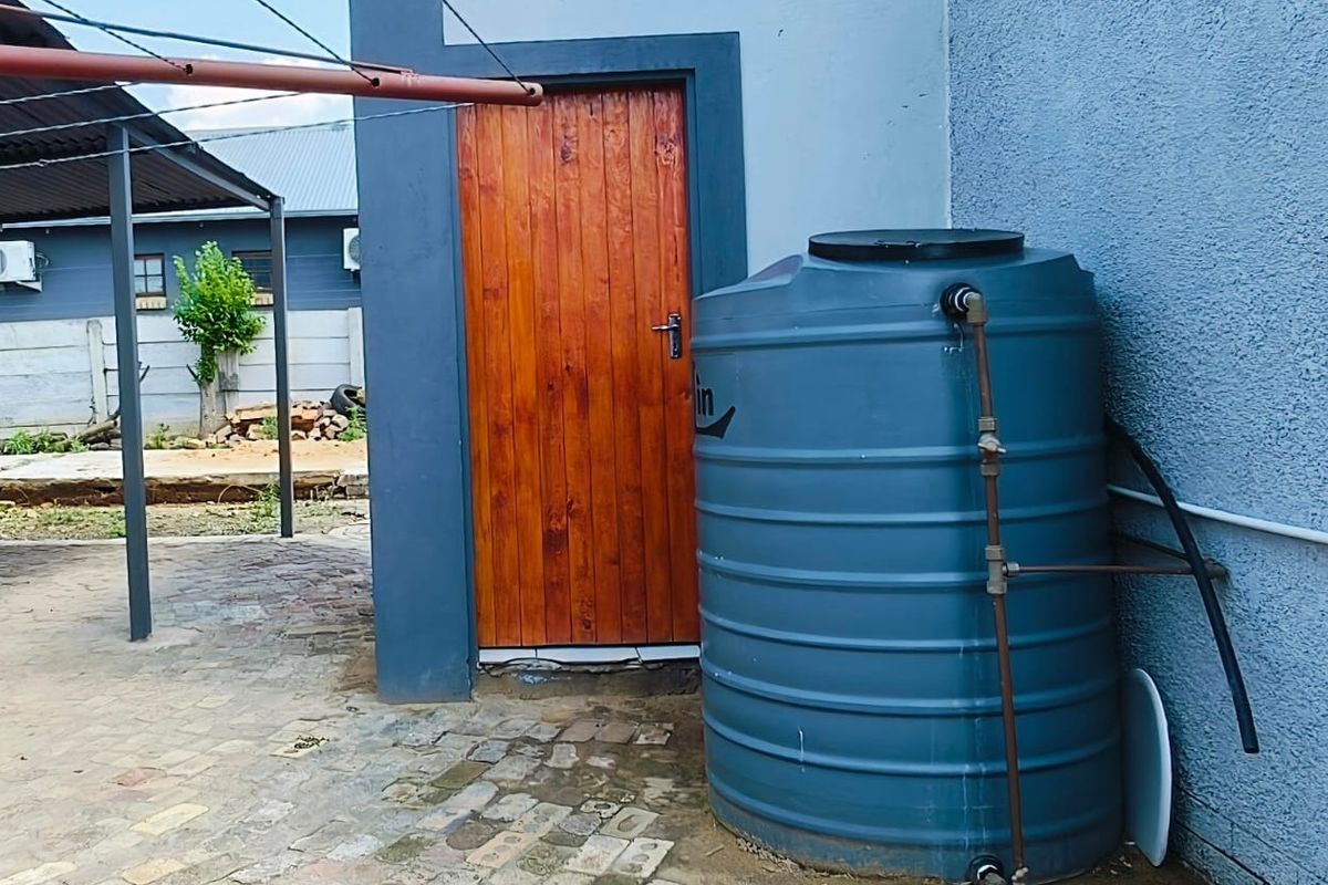 Rear exterior area featuring a water storage tank, a timber door, and a paved courtyard space with an adjacent carport structure.