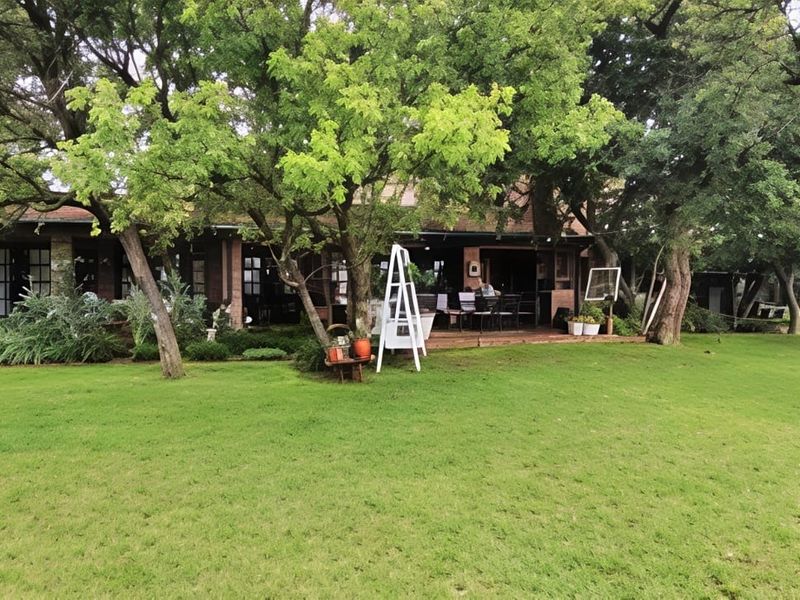 A view of the rear of the house featuring a brick facade, a covered patio area, and a spacious, well-maintained garden with mature trees.