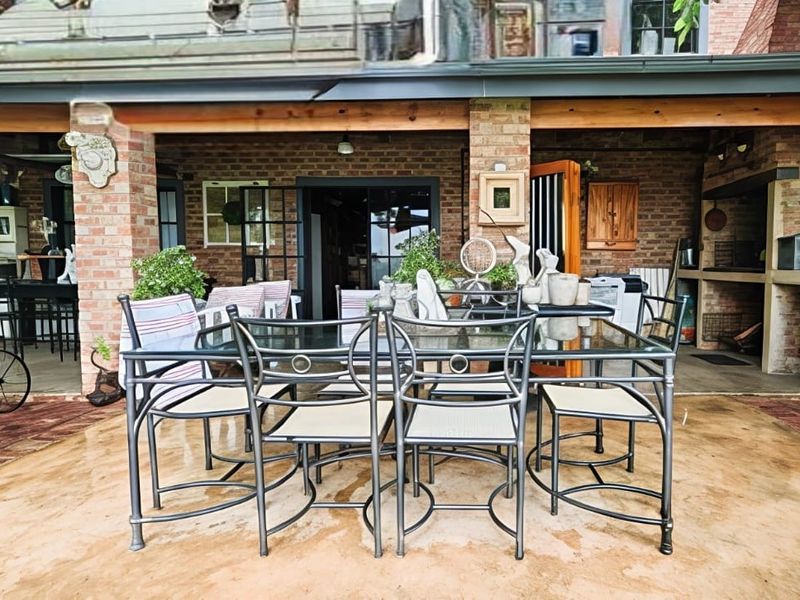 A spacious covered patio featuring exposed brickwork, a built-in braai, and direct access to the interior through sliding glass doors.