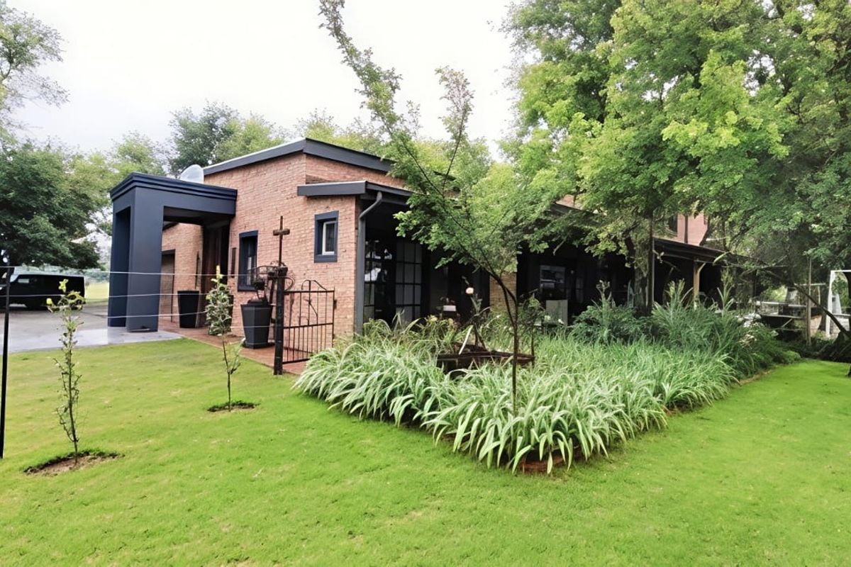 A well-maintained brick house featuring a covered patio area, established garden landscaping, and a paved driveway.