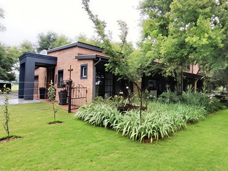 A well-maintained brick house featuring a covered patio area, established garden landscaping, and a paved driveway.