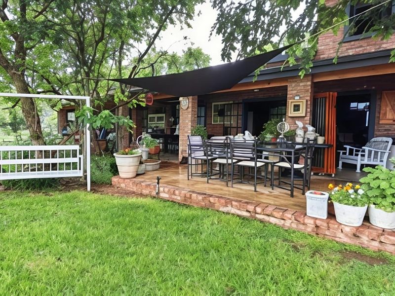 A charming covered brick patio area featuring a shade sail, overlooking a lush green garden with mature trees.