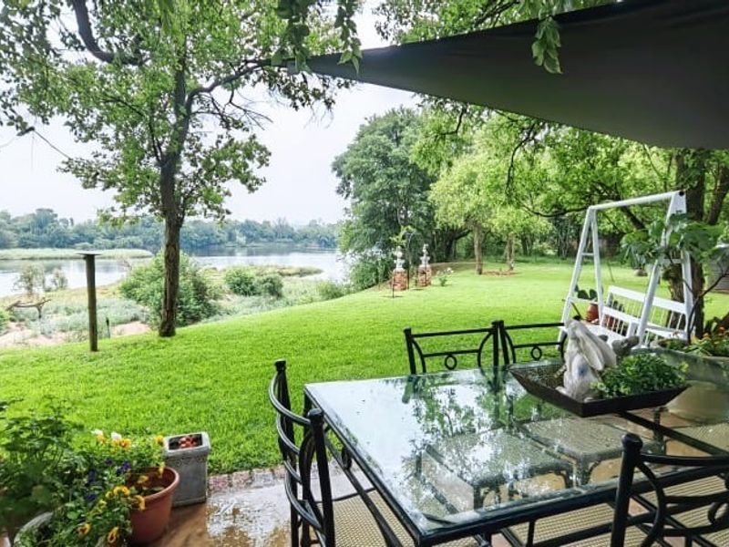 A covered patio area overlooking a lush green garden and a scenic river view, providing a peaceful outdoor living space.