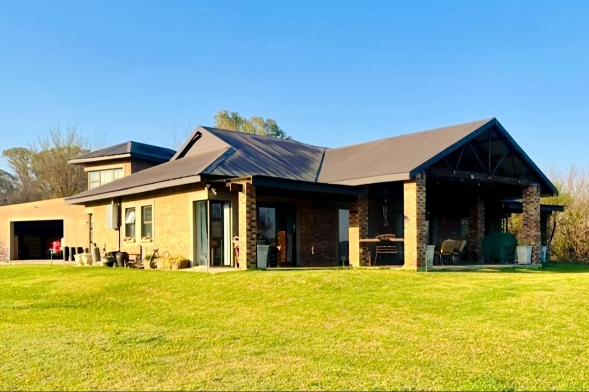 A spacious rear view of the brick house featuring a large covered patio area, metal roofing, and an attached garage set on a grassy lawn.