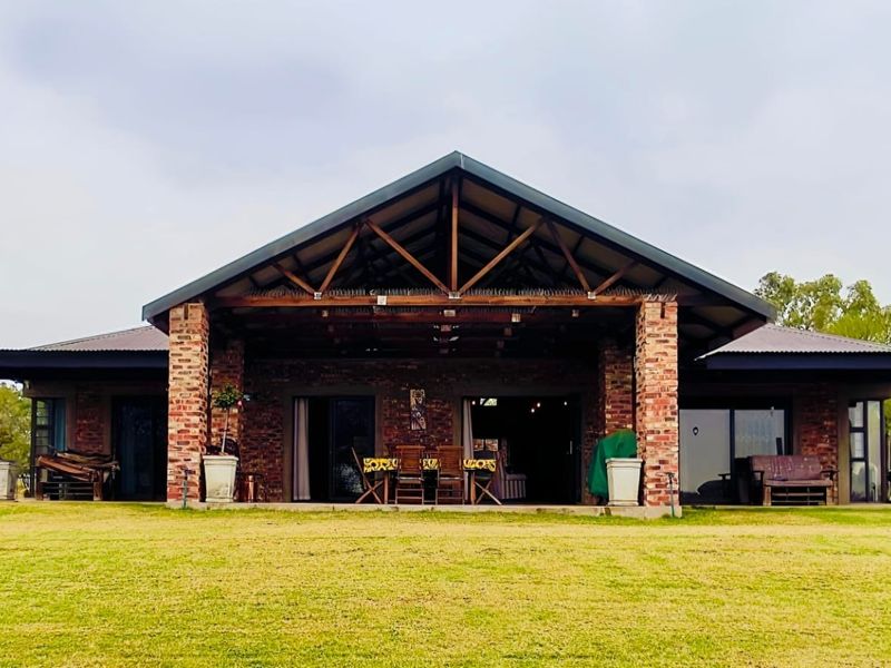A spacious rear exterior view of a brick house featuring a large covered patio with exposed timber trusses and expansive lawn area.