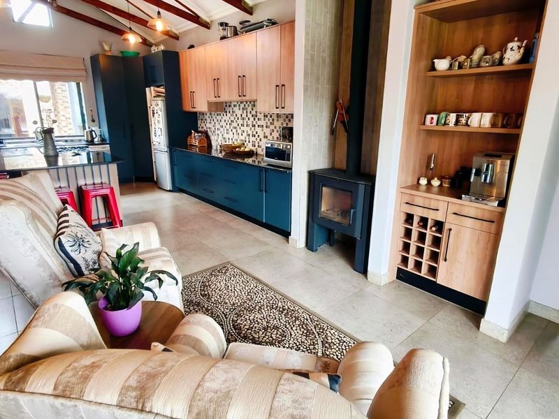 Spacious open-plan living and kitchen area featuring modern cabinetry, a wood-burning fireplace, exposed timber beams, and tiled flooring throughout.