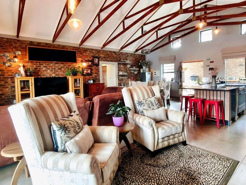 Spacious open-plan living and kitchen area featuring high vaulted ceilings with exposed timber trusses and a striking exposed brick feature wall.