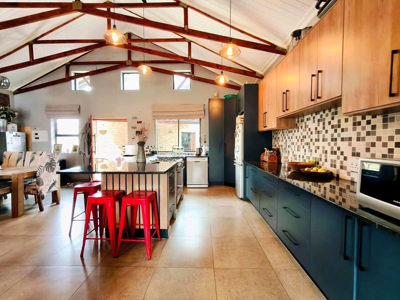 Spacious open-plan kitchen featuring vaulted ceilings with exposed timber trusses, granite countertops, modern cabinetry, and a central island with breakfast bar seating.