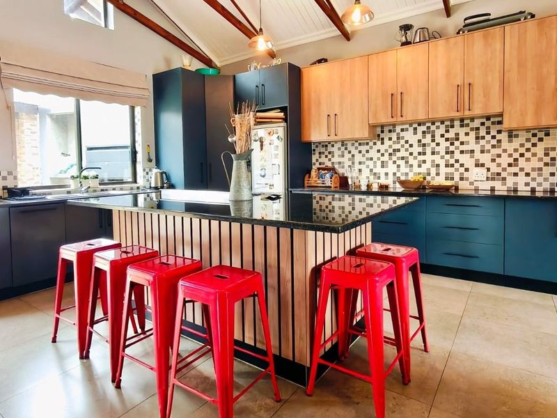 Modern kitchen featuring a central island with granite countertops, two-tone cabinetry, tiled backsplash, and vaulted ceilings with exposed timber beams.