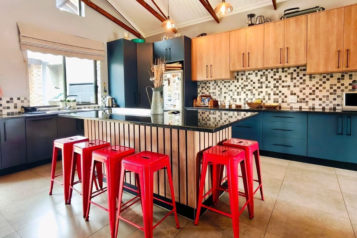 Modern kitchen featuring a central island with granite countertops, two-tone cabinetry, tiled backsplash, and vaulted ceilings with exposed timber beams.