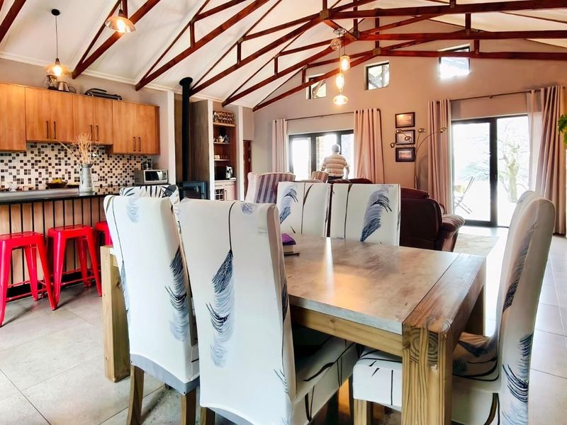 Spacious open-plan living and kitchen area featuring high vaulted ceilings with exposed timber trusses, tiled floors, and direct access to the outdoors.