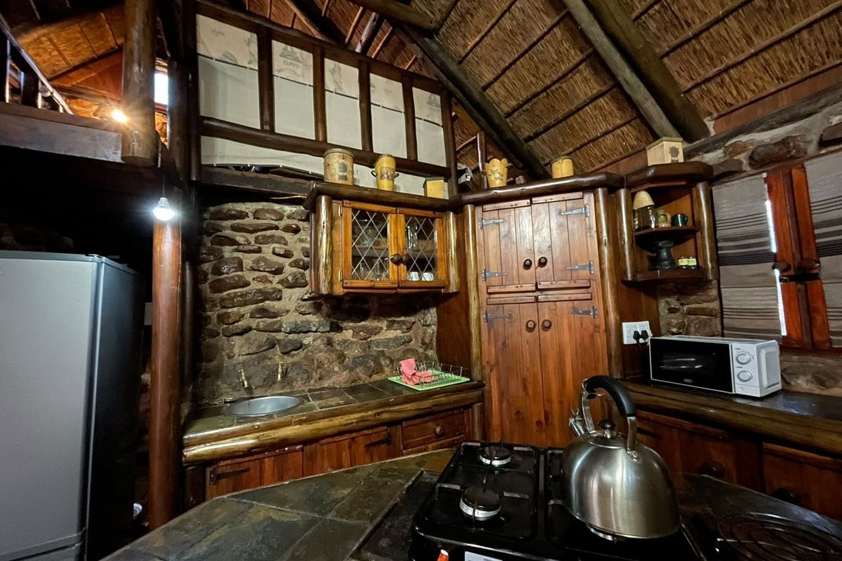 Rustic kitchen featuring exposed timber beams, a thatched ceiling, stone wall accents, and custom timber cabinetry with stone countertops.
